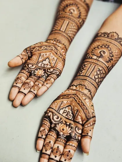 This engagement mehendi features personalized initials 'PR' within a heart, surrounded by lotus and peacock motifs, blending tradition with a personal touch.