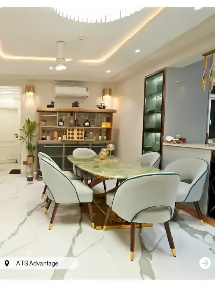 A grand dining area with a green marble table and plush grey chairs. The space is anchored by a stylish bar cabinet and a modern, sculptural chandelier.