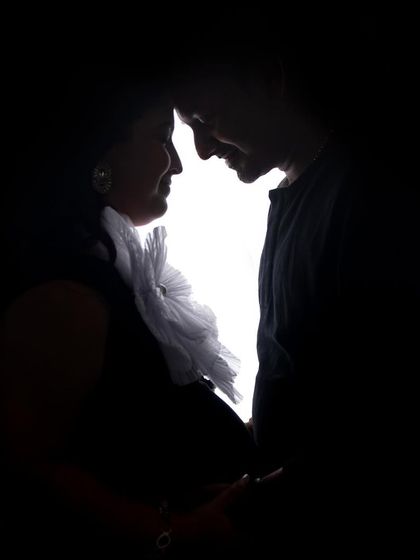 An intimate low-key silhouette of a couple. The light source is behind them, creating a beautiful outline as they share a quiet moment, forehead to forehead.