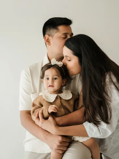 A classic family portrait with both parents kissing their daughter's head. This pose is a beautiful way to show family unity and affection.