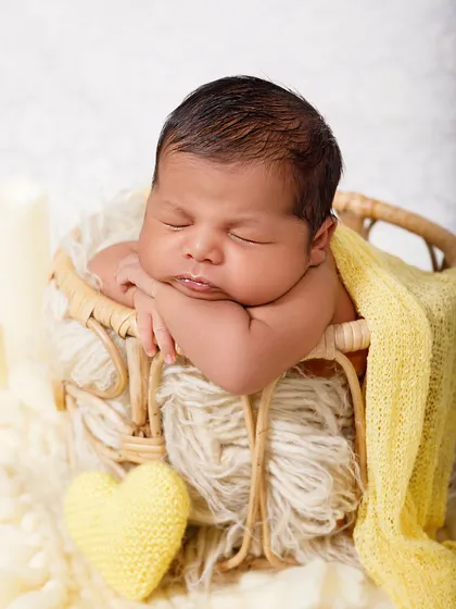 This adorable newborn rests their head on their hands while sleeping in a wicker basket, looking perfectly content.