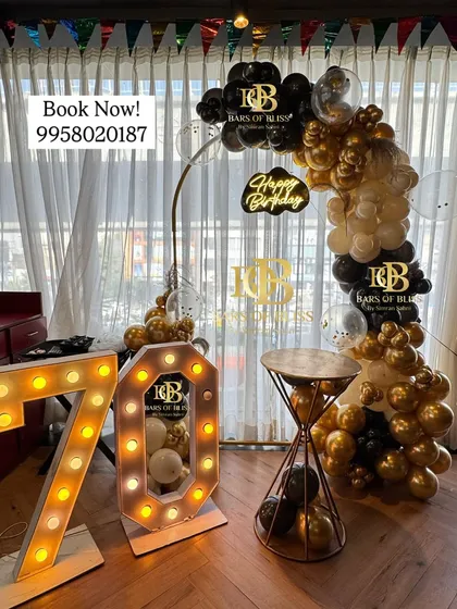 Celebrating a 70th birthday with classic black and gold decor. This setup includes a balloon half-arch, a 'Happy Birthday' neon sign, and large marquee numbers, creating a timeless and celebratory look.