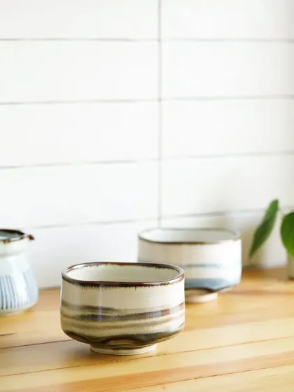 Minimalist styling of two Japanese-style ceramic tea bowls on a wooden surface, creating a calm and serene aesthetic.