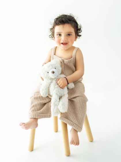 A baby and their bear, a timeless friendship. This portrait showcases a simple, neutral-toned setup that complements the baby's natural charm, making for a classic and heartfelt photograph.