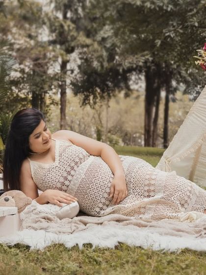 A serene moment from a boho-themed picnic shoot. The expecting mother lies comfortably on a soft blanket, surrounded by rustic props and a teepee, gently cradling her bump.