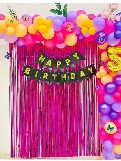 A vibrant 5th birthday decoration with a bright pink foil curtain and a multi-colored balloon arch with butterfly accents.