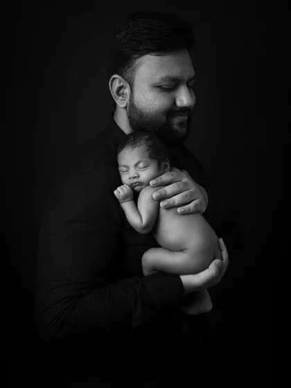 A low-key portrait of a father holding his newborn. The dramatic lighting carves out their forms, creating a powerful and emotional image of paternal love.