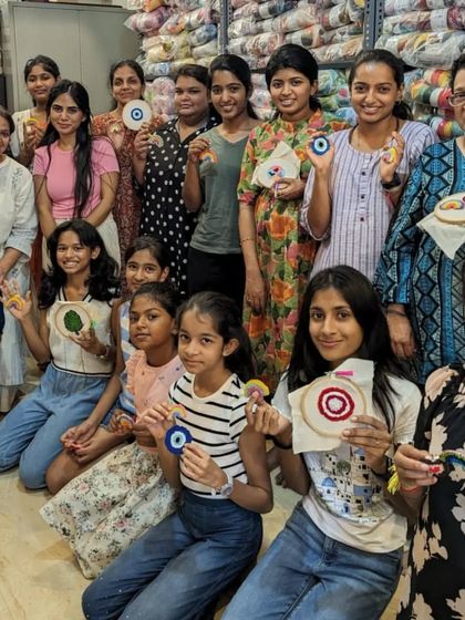 A large group of happy crafters, kids and adults alike, showing off their diverse set of punch needle creations.