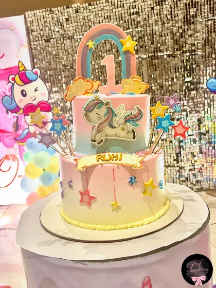 A close-up of the two-tiered unicorn birthday cake for Ruhi. It's adorned with stars, a rainbow, and a cute winged unicorn, perfectly matching the party's theme.