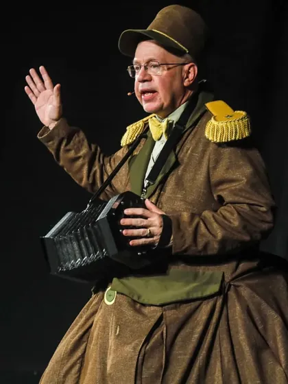 The puppeteer from 'Penguin in my Pocket' plays a concertina, adding live music to the performance and enhancing the magical atmosphere.