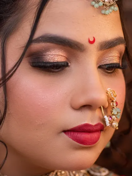 A detailed shot of the eye makeup, featuring shimmering gold tones, a sharp wing, and the classic crescent bindi.