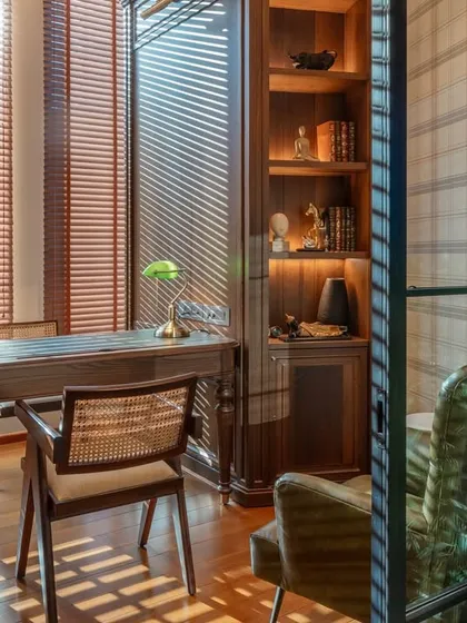 A quiet corner in the office designed as a personal workspace. The combination of a classic wooden desk, a cane-back chair, and natural light filtering through the blinds creates a calm and inspiring atmosphere for focused work.