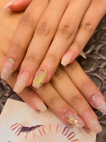Long, coffin-shaped nails with a sheer nude base. The accent nails feature chunky, iridescent glitter flakes and rhinestone details at the cuticle for a dazzling effect.