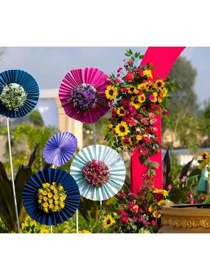 Colorful paper fans with floral centers, a whimsical and creative decor detail for a vibrant Haldi ceremony.