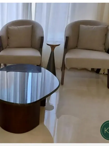 A close-up of the seating arrangement, highlighting the contrast between the dark sofa and the light armchairs. The organic shape of the coffee table adds a soft, modern touch to the room's geometry.