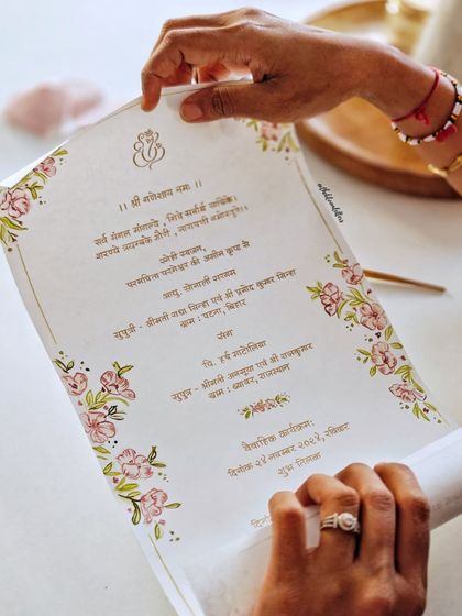 Holding the finished Devanagari invitation. The combination of hand-painted florals and handwritten script on high-quality paper creates a piece that is both beautiful to see and to touch.