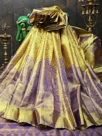 A majestic Banarasi silk saree in a unique combination of gold and purple. The body is covered in intricate peacock motifs, a symbol of royalty and grace in Indian textiles.