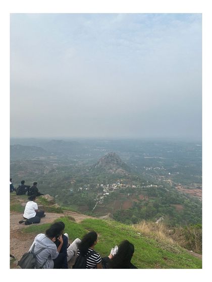 Trekkers sitting at the edge of the Huthridurga viewpoint, looking out at the landscape below.