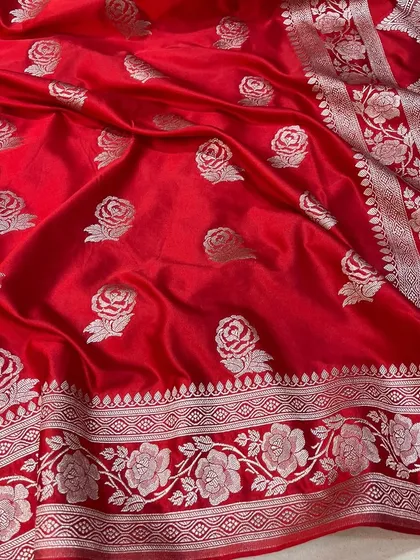 The vibrant red of this Banarasi Mashru silk saree is simply stunning. The silver rose motifs are woven directly into the fabric, creating a luxurious texture and timeless appeal for bridal or festive wear.