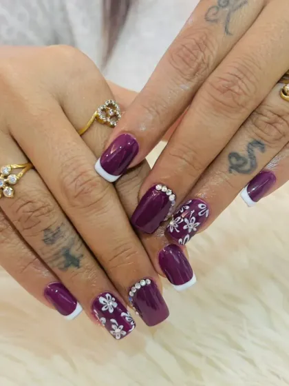 A deep purple manicure with hand-painted white flowers. This design also incorporates French tips and rhinestone accents for extra flair.
