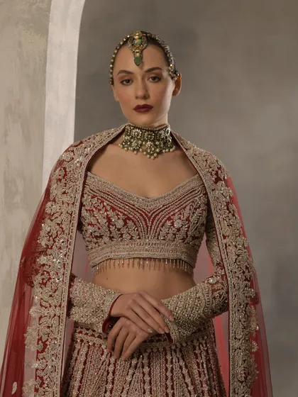 A closer view of a bridal look, highlighting the detailed embroidery on the blouse and the statement choker. The styling choice to drape the dupatta like a cape adds a contemporary edge to the traditional red lehenga.