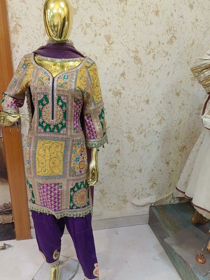 A vibrant multi-colored phulkari style embroidered suit on a mannequin. This is a rich and traditional piece, perfect for a wedding guest.