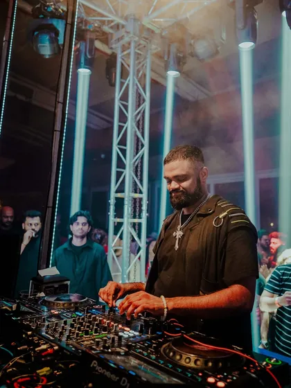 A smiling shot of me at the decks, with cool blue-green light beams in the background. This shows the happier, more melodic side of my sets.