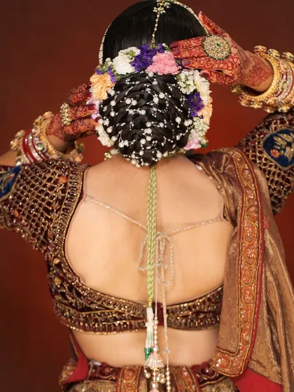 An intricate and traditional bridal bun, heavily embellished with fresh flowers and pearl accessories. This hairstyle is a work of art and perfect for a grand wedding look.