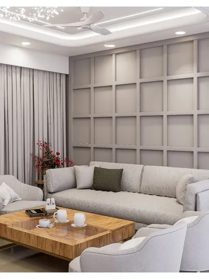 A living room with a sophisticated grey color palette. The wall features classic paneling, creating a timeless backdrop for the comfortable sofa and modern armchairs.