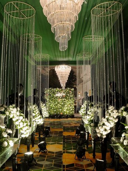 An elegant Sangeet entrance combining lush greenery with sparkling crystal details. Cascading crystal strings hang from the ceiling, leading to a stunning floral wall.