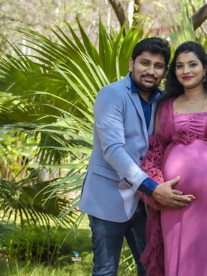 A happy couple announces "It's a boy" in a sunny, tropical-looking park. The vibrant colors of the setting and their outfits make this a cheerful and bright portrait.