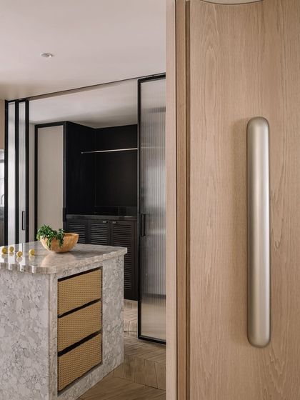A view from the dining area into the kitchen, showcasing the marble island with woven drawer details and the fluted glass partition.
