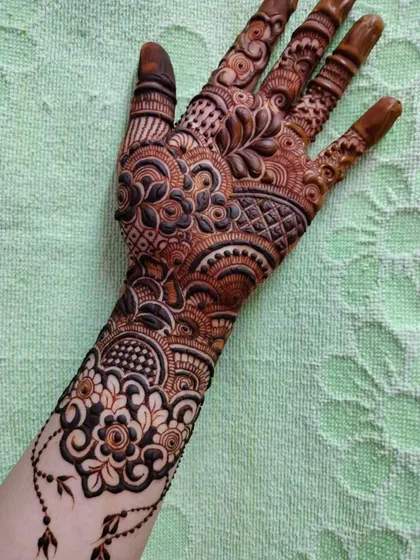 A beautiful design for the back of the hand, featuring a mix of floral and paisley motifs with a delicate, dangling charm element.