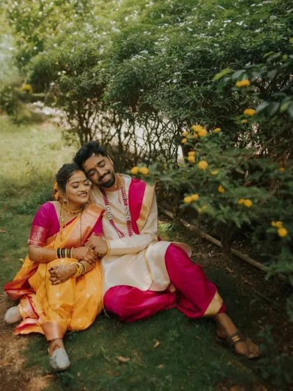 A peaceful moment shared under the shade of flowering bushes. The couple's relaxed posture and content expressions create a serene and romantic scene, highlighting their colorful traditional outfits.