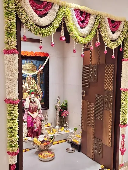 Simple and beautiful Varamahalakshmi habba decor for a home pooja room. The door frame is decorated with a thick garland of flowers, creating a sacred and festive entrance.