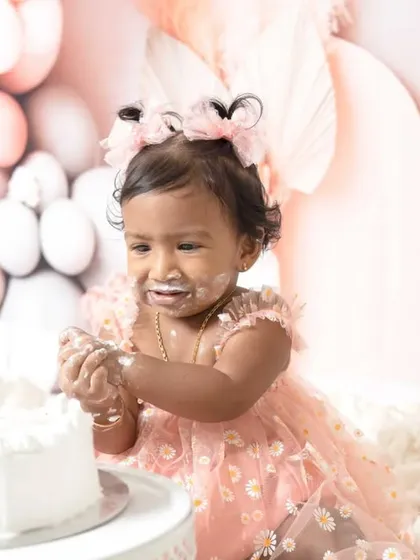 A sweet one-year-old girl enjoying her pink-themed cake smash session. I love capturing these close-ups of their frosting-covered fingers and happy faces.