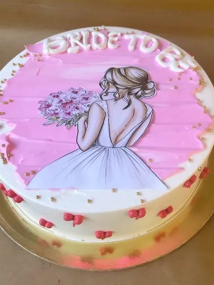 An elegant cake for a "Bride to be." The design features a beautiful illustration of a bride, delicate gold sprinkles, and tiny red bows, making it a perfect centerpiece for a bridal shower.