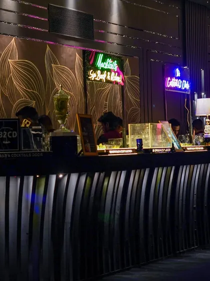 A closer look at the stylish bar, where neon signs for 'Mocktails' and 'The Cocktail O' Clock' add a fun, modern touch to the sophisticated design.