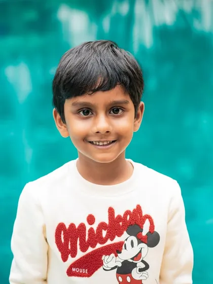 A classic headshot of a smiling boy against a vibrant blue-green background, taken during an outdoor session.