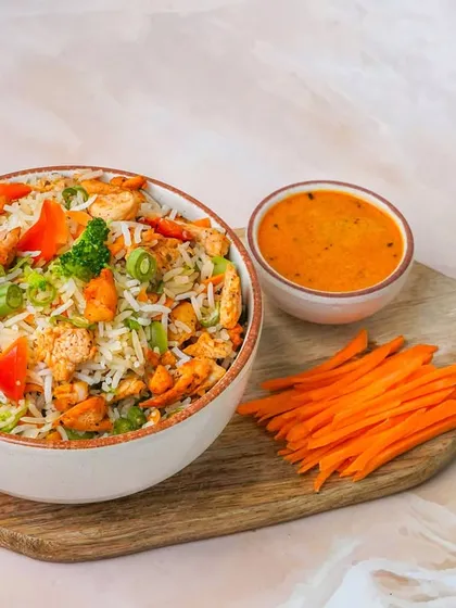 A protein-rich chicken and vegetable rice bowl, presented simply on a wooden board. The focus is entirely on the food, making it a great choice for a straightforward menu photograph.