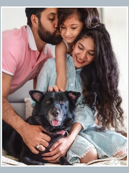 A beautiful, warm portrait of a family sharing kisses and cuddles with their black indie dog, Pakodi. This image radiates love and the close-knit bond they all share.