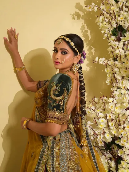 This side profile highlights the intricate hairstyle and the elegant drape of the dupatta. The makeup is kept subtle and clean to balance the richness of the outfit and heavy jewelry.