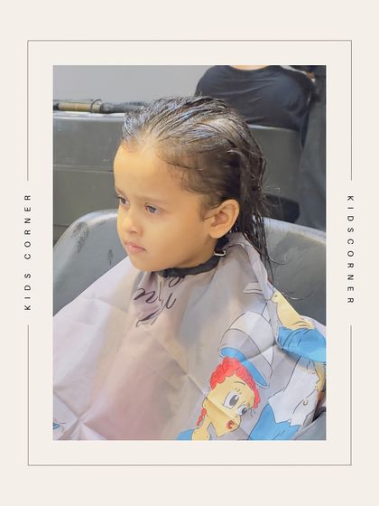 A young client sits patiently in the styling chair, ready for her haircut. The cartoon-themed cape adds a touch of fun to the experience.