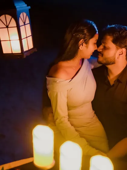 An intimate moment from a romantic dinner shoot. The couple leans in close, illuminated by the soft glow of candles and a lantern, creating a warm and passionate atmosphere.