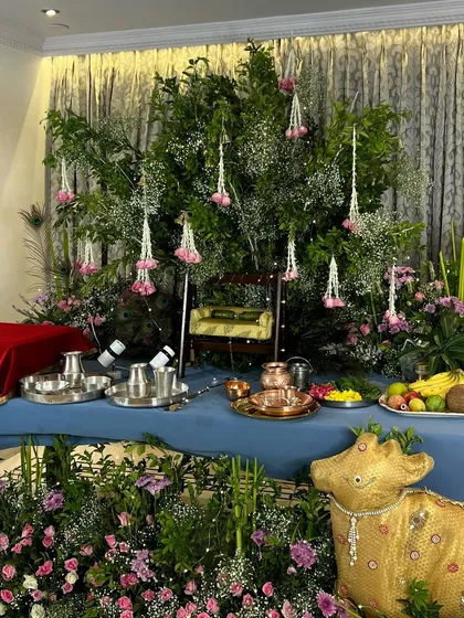A complete view of our elegant Janmashtami setup. The altar table is draped in blue fabric, with a backdrop of lush green foliage and hanging floral tassels, creating a serene and beautiful space for worship.