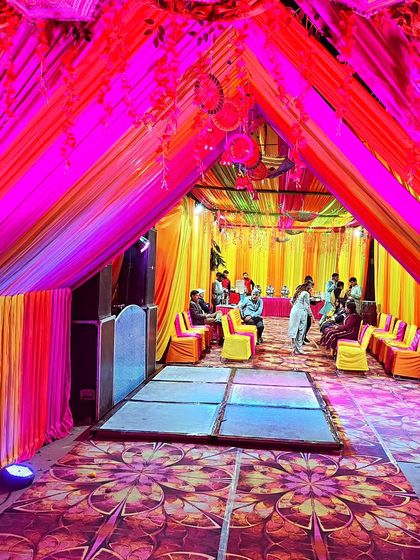 The interior of a Mehendi night tent, illuminated with vibrant pink and yellow lights, featuring a dance floor and guest seating.