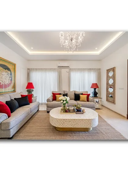 A bright and spacious living room featuring a large traditional painting as a focal point. The neutral sofas are accented with red and black pillows, creating a balanced composition that is both elegant and inviting.