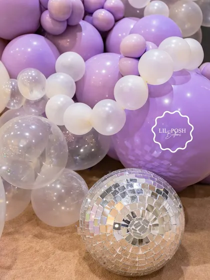 A disco ball and clear bubble balloons add a touch of sparkle and fun to the purple balloon garland at the mermaid party.