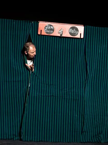 The puppeteer peeks through the curtains of his booth, a classic trope in this style of interactive hand puppet theatre.