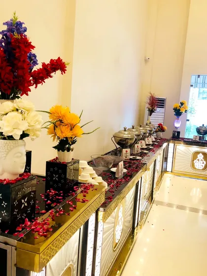 A stunning buffet display with vibrant floral arrangements, including a unique Buddha head vase. The counter is adorned with red rose petals, adding a touch of romance and elegance to the setup.